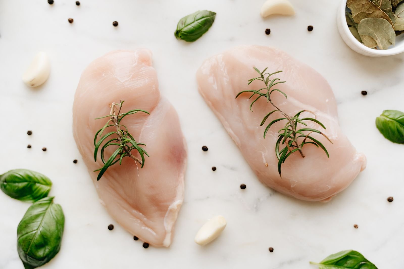 Raw chicken breast cuts arranged with herbs on a clean preparation surface